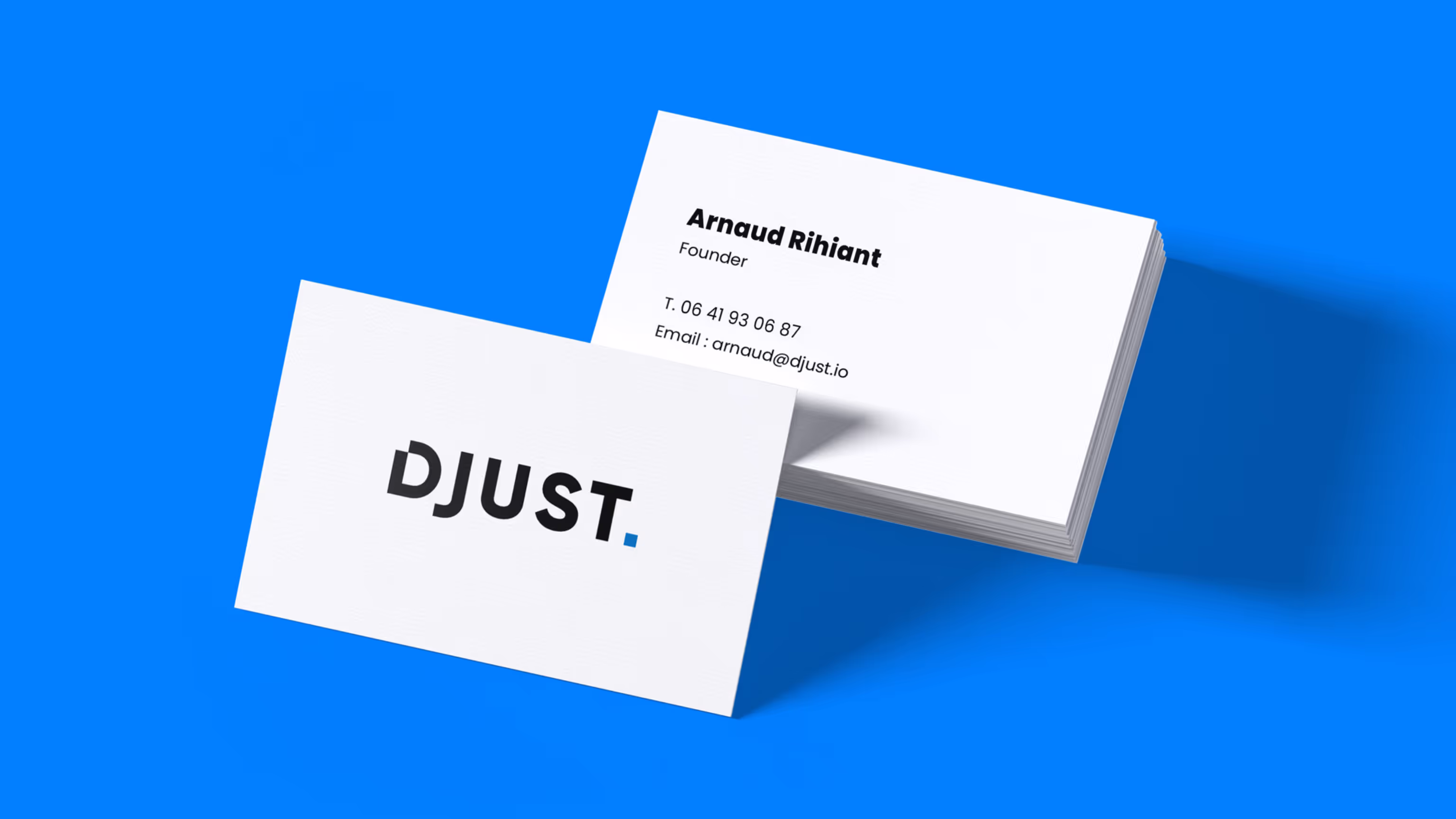 Mock-up of white DJUST business cards on a blue background, showing the logo on the front and Arnaud Rihiant's contact details on the back