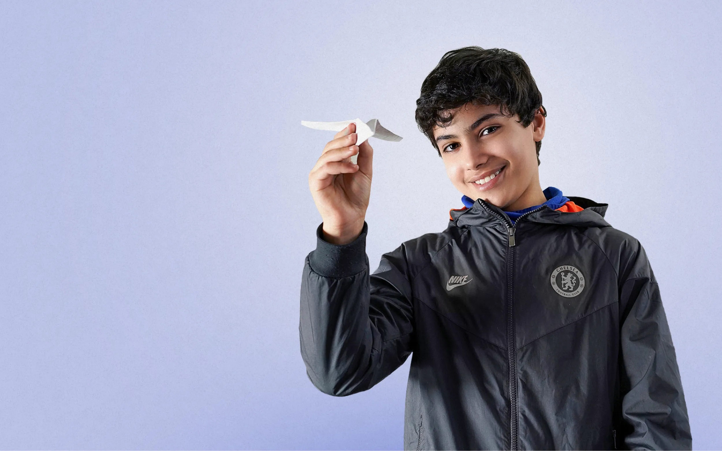 Jeune homme en veste sportive tenant un avion en papier, fond parme clair, visuel hero site web Fondation Sycomore